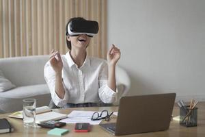 senhora empreendedora no fone de ouvido vr sentado na mesa no escritório em casa interagindo com visualização 3d foto