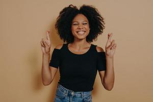 linda e adorável mulher afro-americana posando em roupas casuais enquanto gesticulava o sinal de dedos cruzados foto