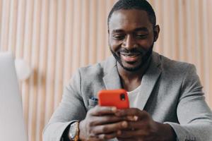 alegre jovem afro-americano conversando online no smartphone olhando na tela do telefone com sorriso foto
