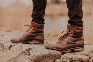 foto recortada de homem irreconhecível usa sapatos velhos, anda ao ar livre, fundo desfocado. botas em pedras. conceito de moda