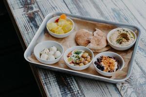 conceito de cozinha tradicional de Israel. vista superior de saborosos pratos exóticos servidos na bandeja. pão pita, legumes na grelha, queijo de cabra, homus na mesa de madeira foto