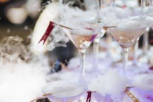 taças de champanhe com fumaça ao redor. reação química do gelo seco com a água. névoa branca de coquetel alcoólico. conceito de recreação e celebração foto