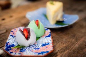 mochi recheado com morangos envoltos em feijão vermelho em um prato de azulejos coloridos estilos japoneses na mesa de madeira. foto