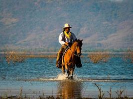 um cowboy ocidental estava montando um cavalo para percorrer a área do lago, com o fundo nas montanhas foto