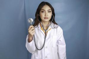 retrato de uma jovem médica asiática, um profissional médico está sorrindo e usando estetoscópio isolado sobre fundo azul foto