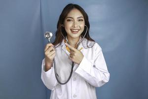 retrato de uma jovem médica asiática, um profissional médico está sorrindo e usando estetoscópio isolado sobre fundo azul foto