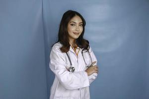retrato de uma médica confiante atraente, braços sorridentes amigáveis cruzados usam estetoscópio de jaleco branco isolado fundo de cor azul foto