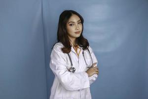 retrato de uma médica confiante atraente, braços sorridentes amigáveis cruzados usam estetoscópio de jaleco branco isolado fundo de cor azul foto