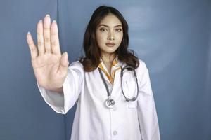 séria médica asiática com estetoscópio e jaleco branco, mostrando o sinal de stop. foto
