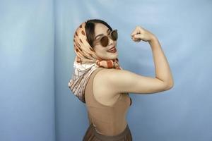 conceito retrô de uma jovem mulher forte asiática mostrando seu bíceps isolado por um fundo azul foto