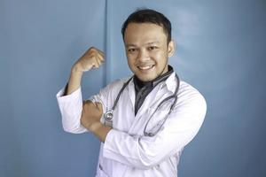 um retrato de um jovem médico asiático mostrando seu bíceps isolado por um fundo azul foto