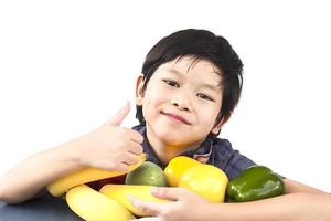 menino saudável asiático mostrando expressão feliz com variedade colorida de frutas e vegetais sobre fundo branco foto