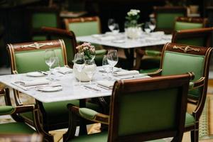 mesa servida com copos de luxo, talheres, flores, cadeiras verdes ao redor no restaurante aconchegante. ninguém em tiro. mesa decorada para evento festivo foto