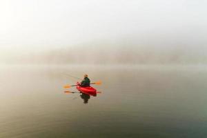pescador no caiaque vermelho, névoa da manhã foto