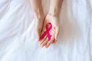 outubro mês de conscientização do câncer de mama, mão de mulher adulta segurando a fita rosa no fundo rosa para apoiar as pessoas que vivem e estão doentes. mulheres internacionais, mãe e conceito de dia mundial do câncer foto