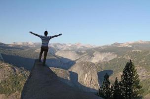 conceito de sucesso - jovem com braços levantados com vista para o parque nacional de yosemite de uma rocha íngreme foto