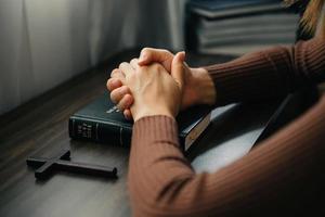 mãos juntas em oração a deus junto com a bíblia no conceito cristão e religião, mulher reza na bíblia na mesa de madeira foto