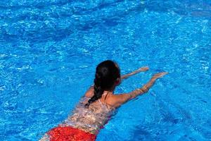 vista superior de uma garota bronzeada, feminina, modelo em um maiô vermelho, nadando na água azul da piscina. foto