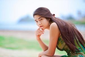 linda menina adolescente biracial sentado na praia tropical, pensando foto