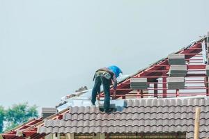 carpinteiro de construção instalando telhas no local de construção da casa foto