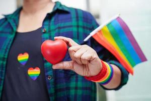 mulher asiática segurando hert vermelho com bandeira do arco-íris, direitos do símbolo lgbt e igualdade de gênero, mês do orgulho lgbt em junho. foto