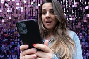 mulher espantada usando telefone celular e fundo roxo brilhante foto