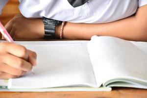 vista frontal do estudante asiático segurando uma caneta na mão e fazendo o teste em sala de aula. conceito para testar, escrever e fazer tarefas e trabalhos de casa. foco seletivo na mão e caneta. foto