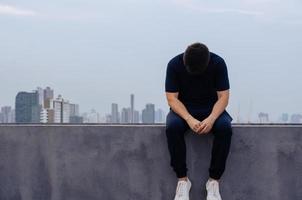 homem deprimido miserável asiático sente-se sozinho com o fundo da cidade. depressão e conceito de saúde mental. foto