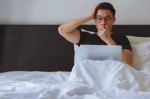 homem asiático assistindo notícias surpresa on-line no computador portátil de manhã na cama. foto