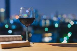um copo de vinho tinto e livro na mesa de madeira.