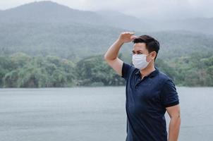 homem asiático usando máscara facial para proteger de ficar doente e molhado da chuva na estação das monções. foto