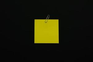 papel de nota em branco amarelo com clipe de papel em fundo escuro. conceito preto plano minimalista leigo. foto