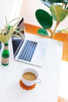 local de trabalho freelancer, laptop, xícara de café e planta em vaso na mesa branca foto