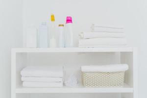 lavanderia com toalhas bem dobradas, garrafas de detergente líquido ou detergente. tudo nas cores brancas. tarefas diárias e dia de lavanderia foto