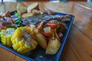 bife grelhado com molho é servido com uma salada de frutas e legumes dentro de um prato de cerâmica preta na mesa da sala de jantar para preparar o bife para um jantar festivo. foto