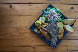 bife grelhado com molho é servido com uma salada de frutas e legumes dentro de um prato de cerâmica preta na mesa da sala de jantar para preparar o bife para um jantar festivo. foto