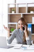 mulher de negócios jovem ao telefone no escritório. mulher de negócios mandando mensagens no telefone e trabalhando no laptop. mulher de negócios muito jovem sentado no local de trabalho. mulher de negócios sorridente. foto