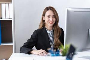 retrato de jovem empresária asiática está feliz em trabalhar no escritório moderno usando um computador portátil. conceito de telemarketing de comércio eletrônico freelance de empregado de negócios. foto