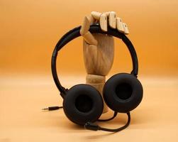 fones de ouvido pretos modernos no display de mão de madeira isolado em fundo laranja. foto