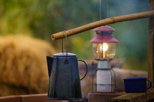caneca de café esmaltada, chaleira vintage em chamas no acampamento noturno. o fundo é uma lanterna de gás antiga. efeito de foco suave focus.shallow. foto