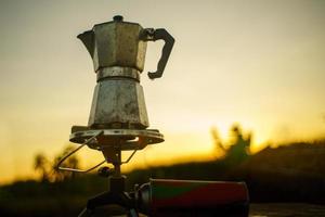 cafeteira antiga no fogão a gás para acampar quando o sol nasce de manhã. foto