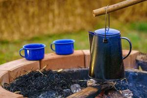chaleira de esmalte vintage no fogão a lenha no acampamento de manhã. chaleira de café antiga. fogueira no campo.foco suave. foto