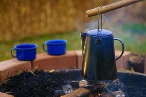 chaleira de esmalte vintage no fogão a lenha no acampamento de manhã. chaleira de café antiga. fogueira no campo.foco suave. foto