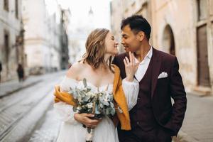 um casal de noivos internacionais, uma noiva europeia e um noivo asiático caminham juntos pela cidade. foto