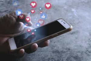 pessoa da ásia usando uma mídia social coloca como e bate-papo com ícone de amor no celular na tela preta do smartphone. conceito de marketing de internet de mídia social. foto