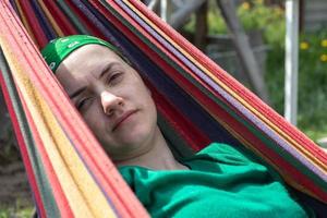 uma mulher de aparência caucasiana encontra-se em uma rede do lado de fora em um parque. relaxando em uma rede, relaxando em um jardim de verão. foto