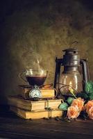 café em copo de vidro em livros antigos e relógio vintage com lanterna de óleo de lâmpada de querosene queimando com luz suave de brilho no piso de madeira envelhecido. foto