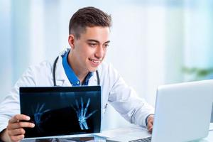 bonito jovem médico revendo resultados no laptop.