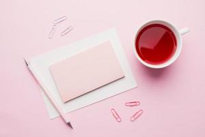 objetos vermelho-rosa. xícara de chá e bloco de notas para texto em fundo rosa pastel. copie o espaço. vista superior plana lay foto