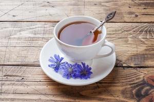 copo com bebida de chicória e flores de chicória azul na mesa de madeira. copie o espaço. foto